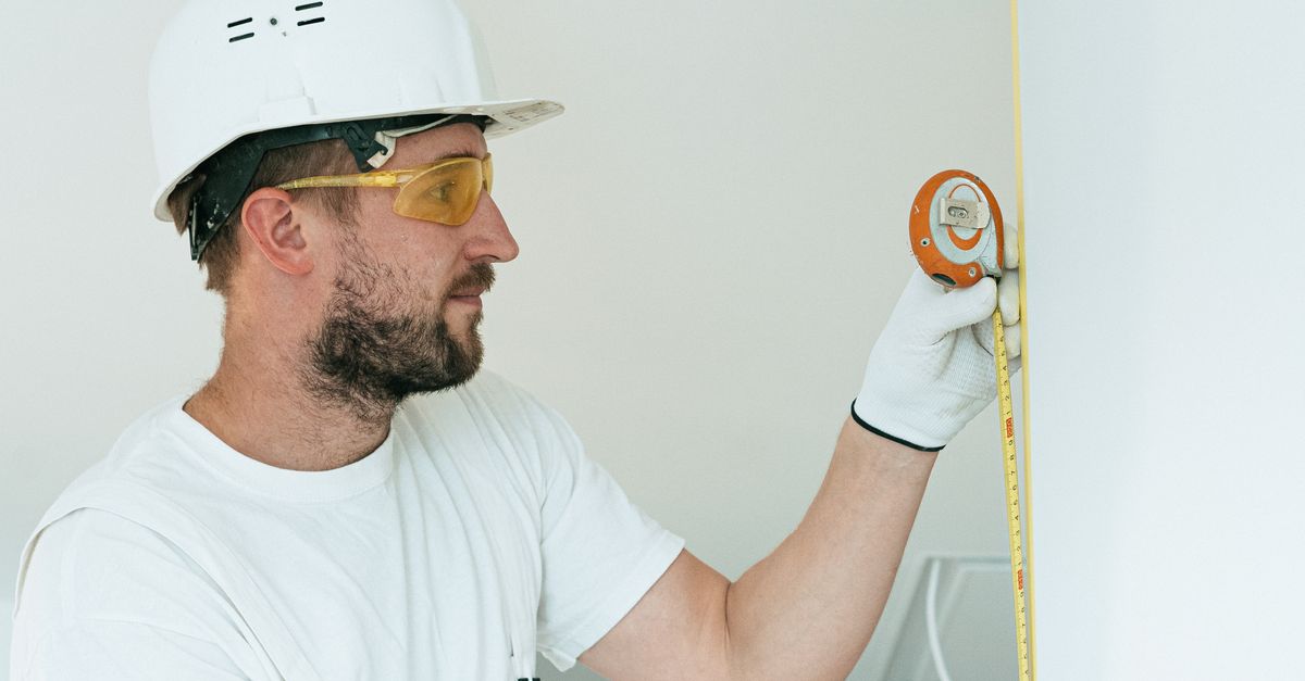 Bausachverständiger misst eine Wand mit einem Maßband